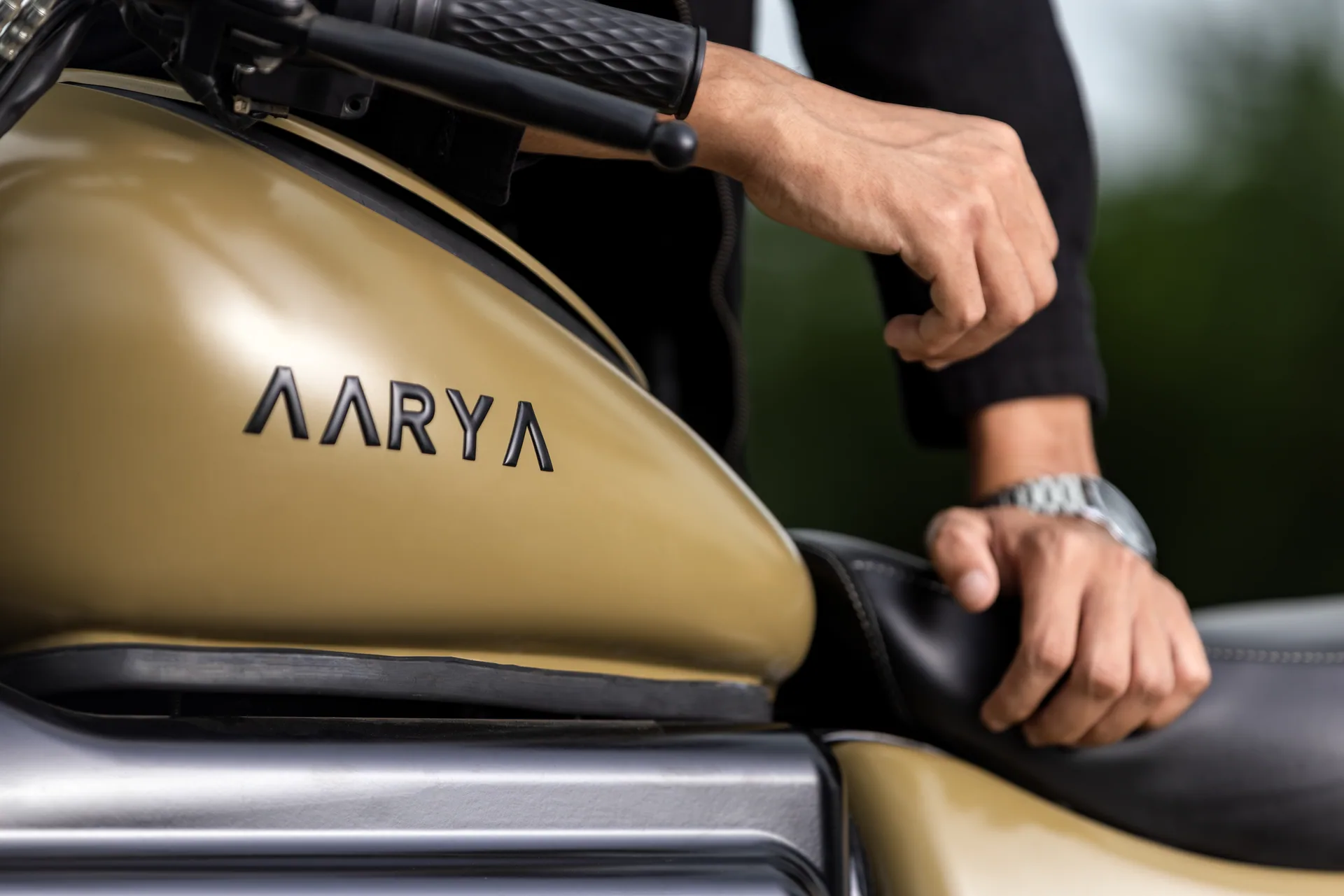 A rider's hands resting on the Aarya Commander fuel tank